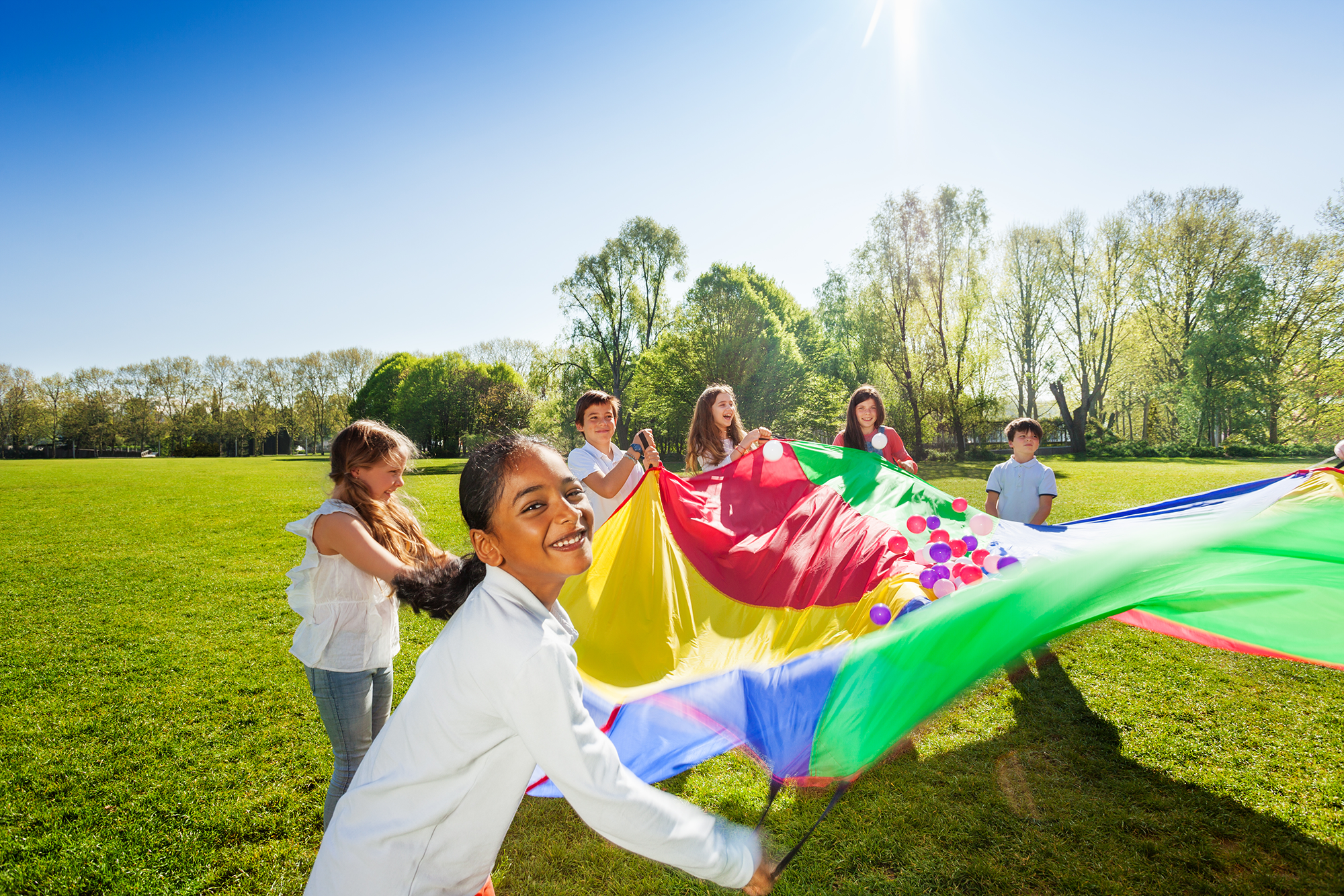 A group of kids playing with a giant parachute outside on the grass