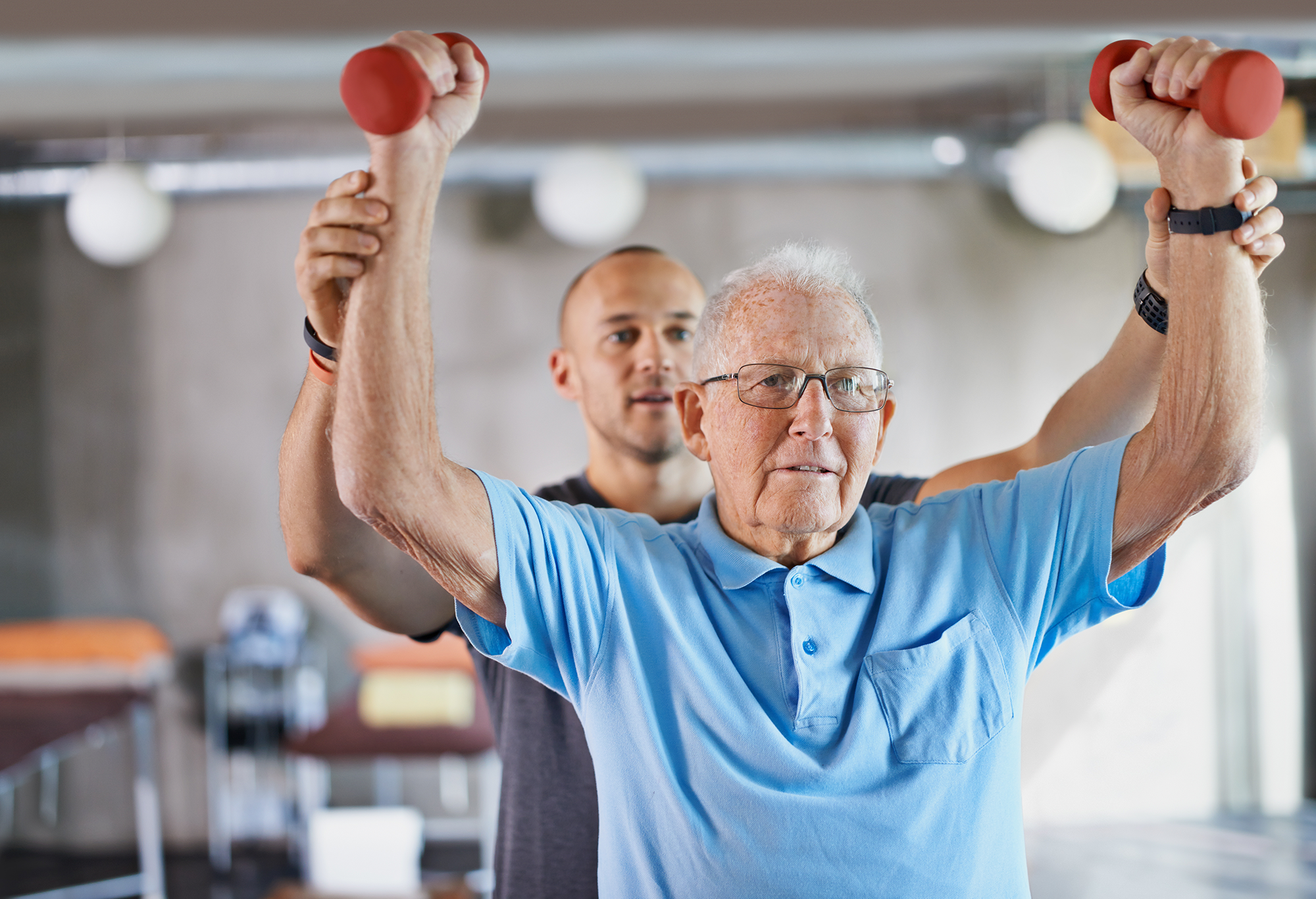 A man training an older man at the gym holding weights